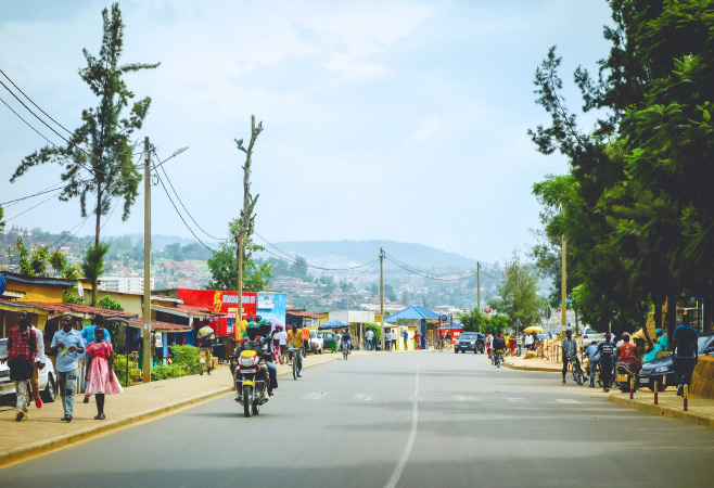 A colorful streetscape with motos, bikes, and people in the outskirts of the capital city, Kigali