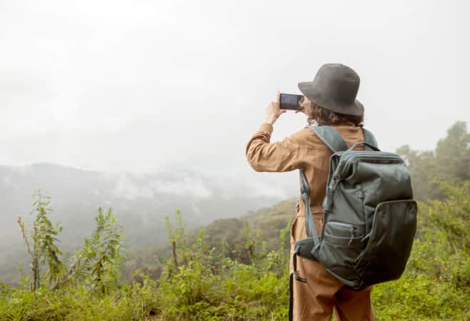 A woman holding a backpack and taking a photo of mountains during travel in Africa